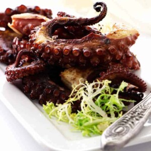 Grilled octopus legs on plate with greens