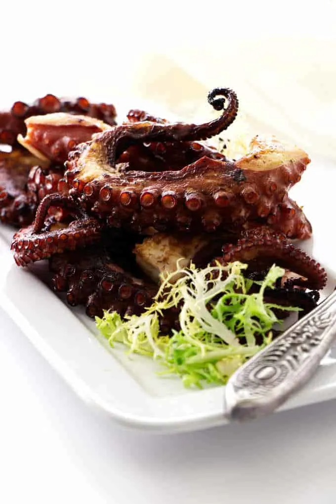 Grilled octopus legs on plate with greens