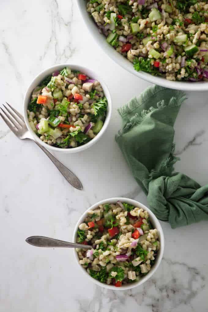 overhead shot of two small servings of barley salad next to a large serving bowl