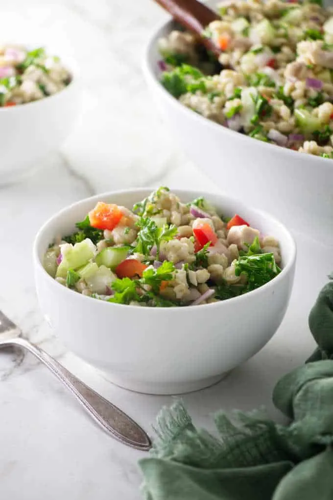 A small bowl of barley salad with a large serving dish in the background