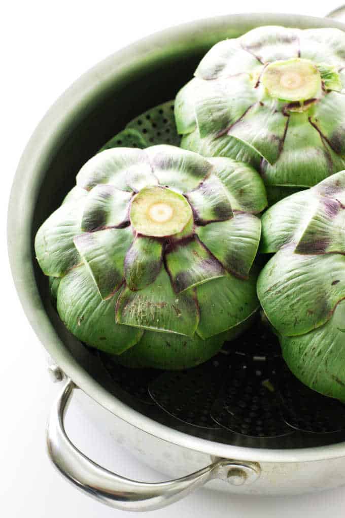 three artichokes in a pot with a steamer basket