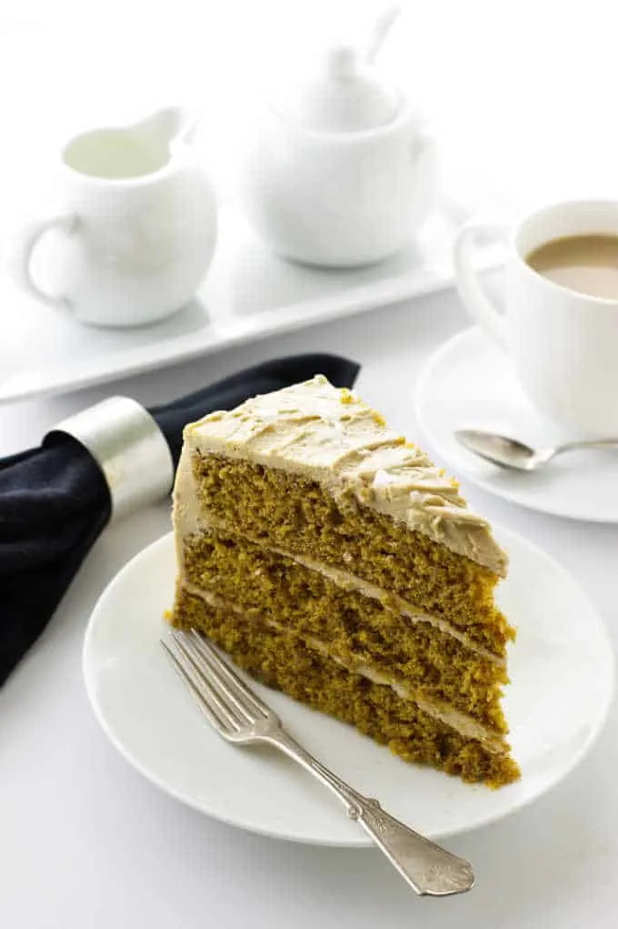 Pumpkin Spice Cake with Salted Caramel Frosting on a plate with fork, cup of coffee, napkin, cream and sugar