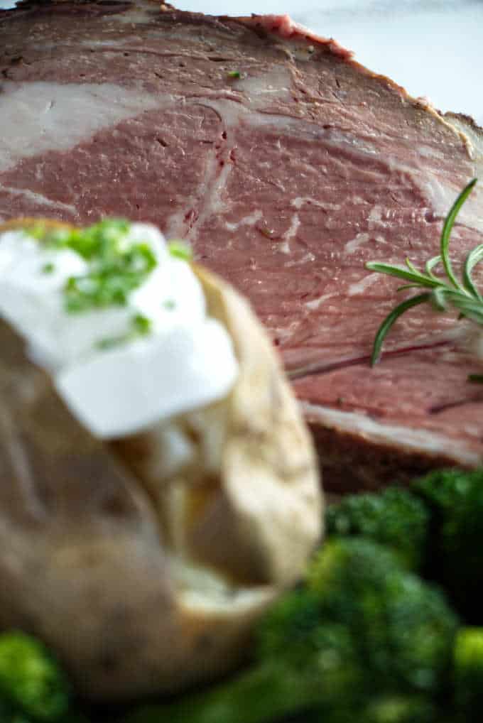 A slice of smoked prime rib with a baked potato and steamed broccoli