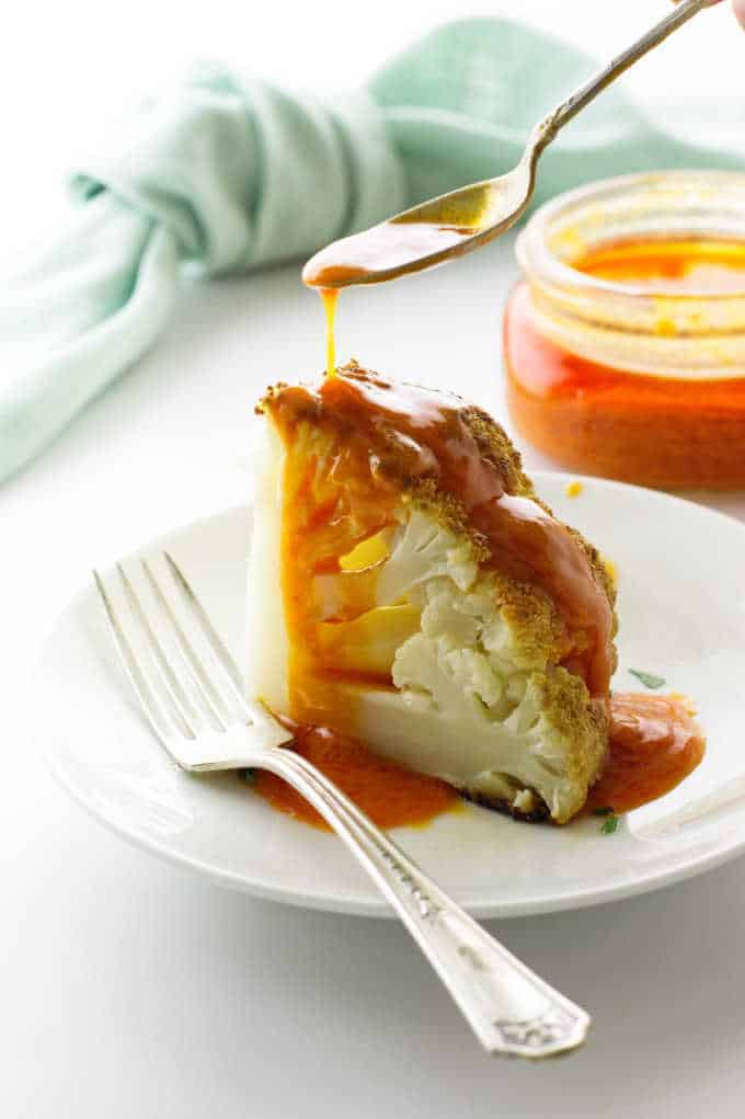 Orange buffalo sauce being drizzled over a roasted wedge of cauliflower.