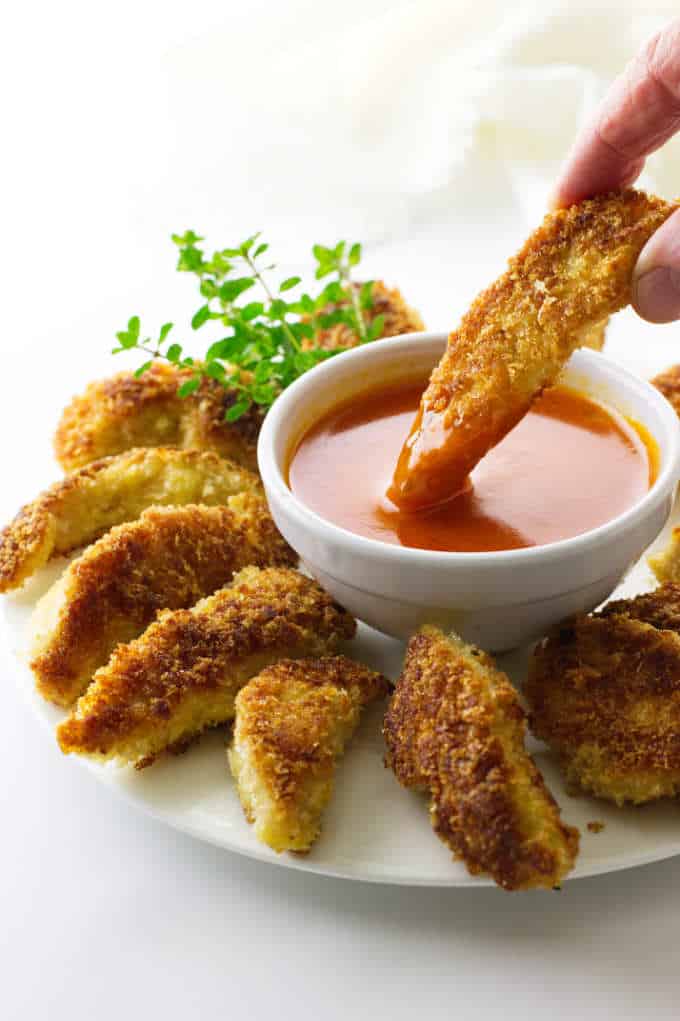 plate of chicken sticks with one being dipped in buffalo sauce