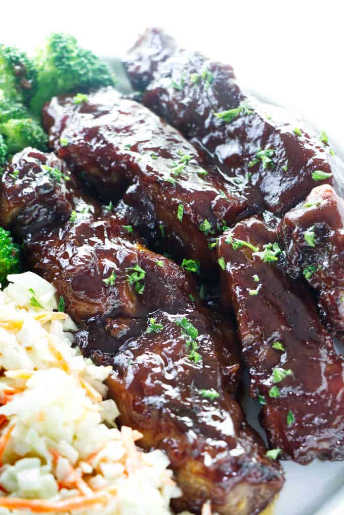 Three country style pork ribs on a plate with a salad and broccoli.