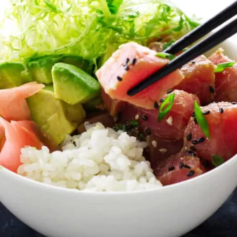 Bowl of tuna poké, chopsticks, avocado, rice and ginger