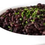 A serving dish with instant pot black beans and some parsley.