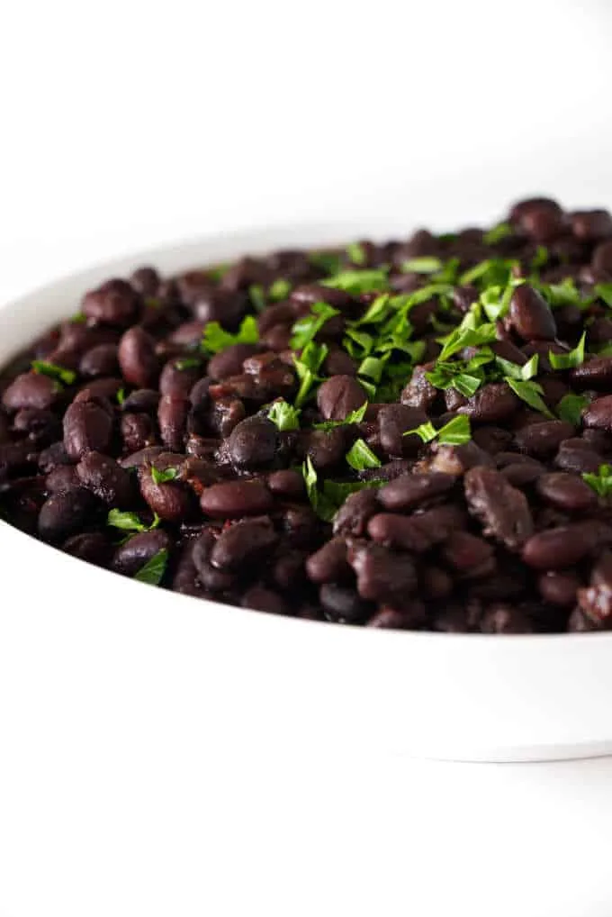 A serving dish with instant pot black beans and some parsley.