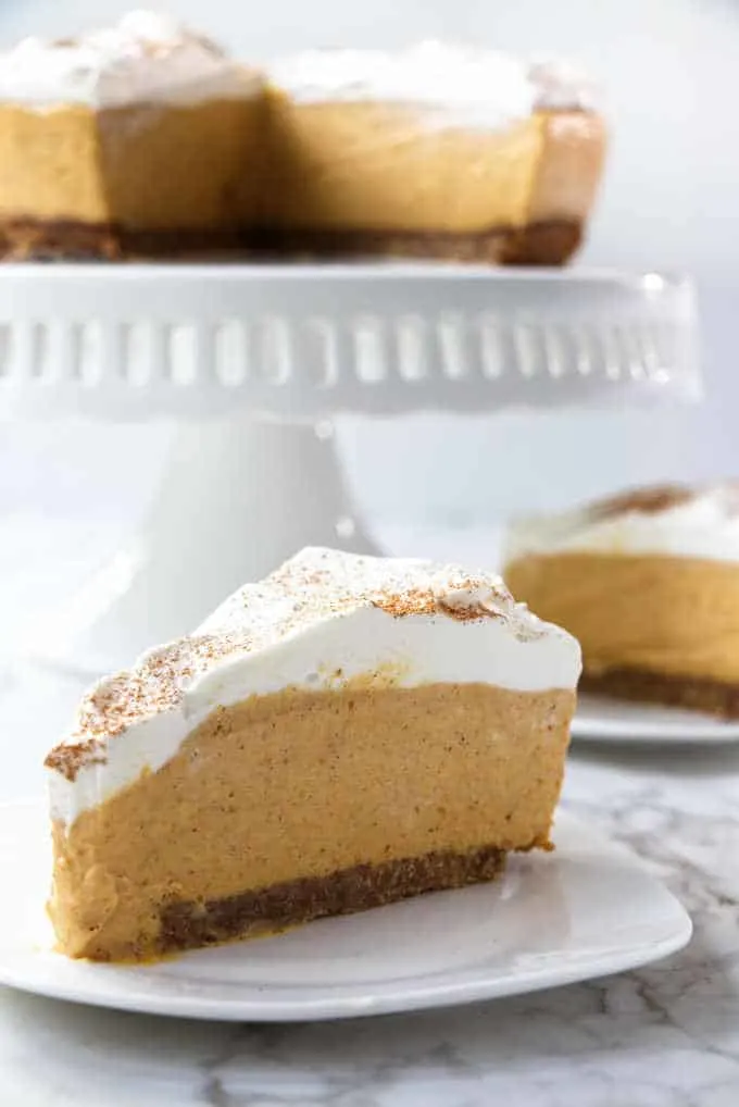 a slice of no-bake pumpkin cheesecake with a full cheesecake in the background
