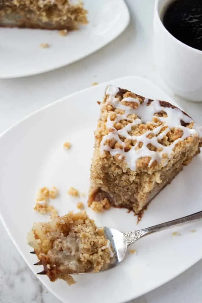 A slice of fresh pear cake with a fork and a cup of coffee.