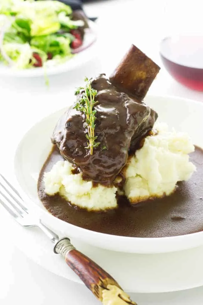 Dish of mashed potatoes in sauce with serving of short ribs