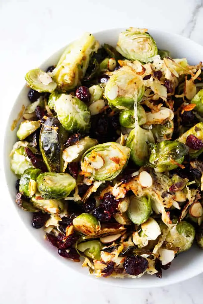 A serving bowl of roasted Brussels sprouts with parmesan, cranberries, and almonds