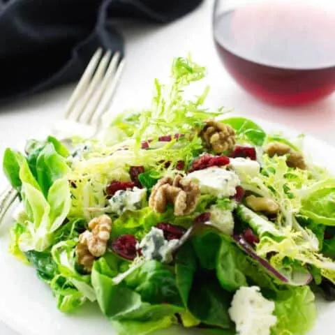 Salad on a plate with fork, napkin and wine in the background