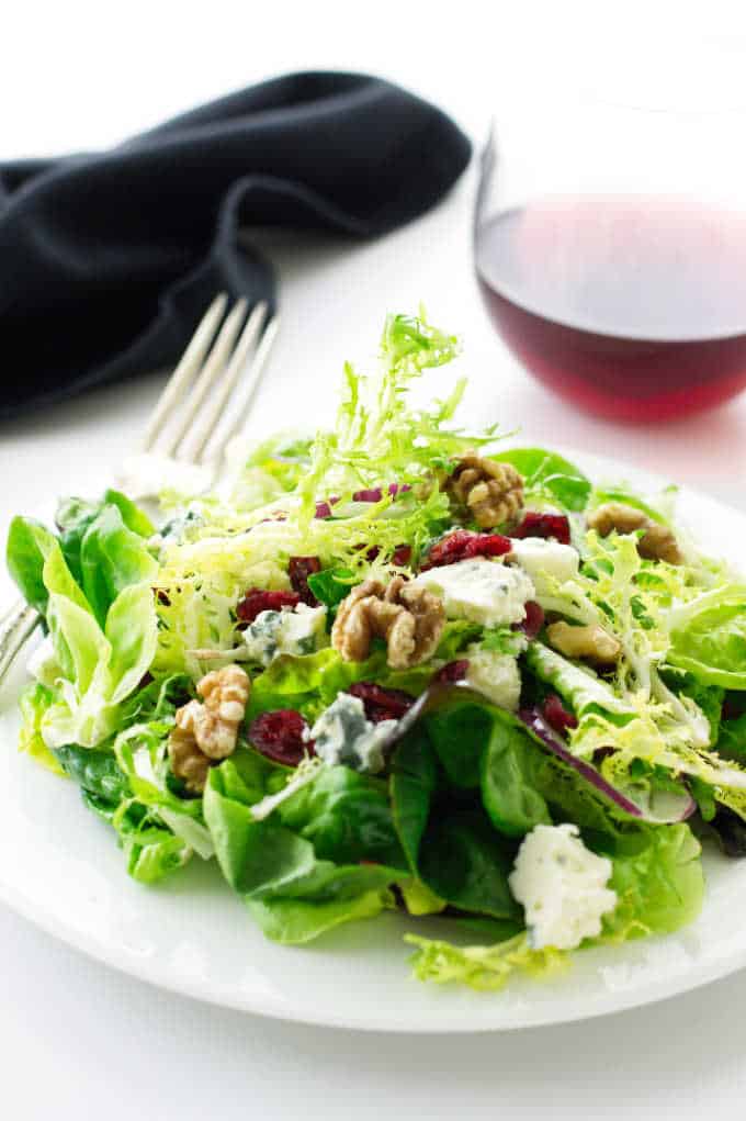 Salad on a plate with fork, napkin and wine in the background