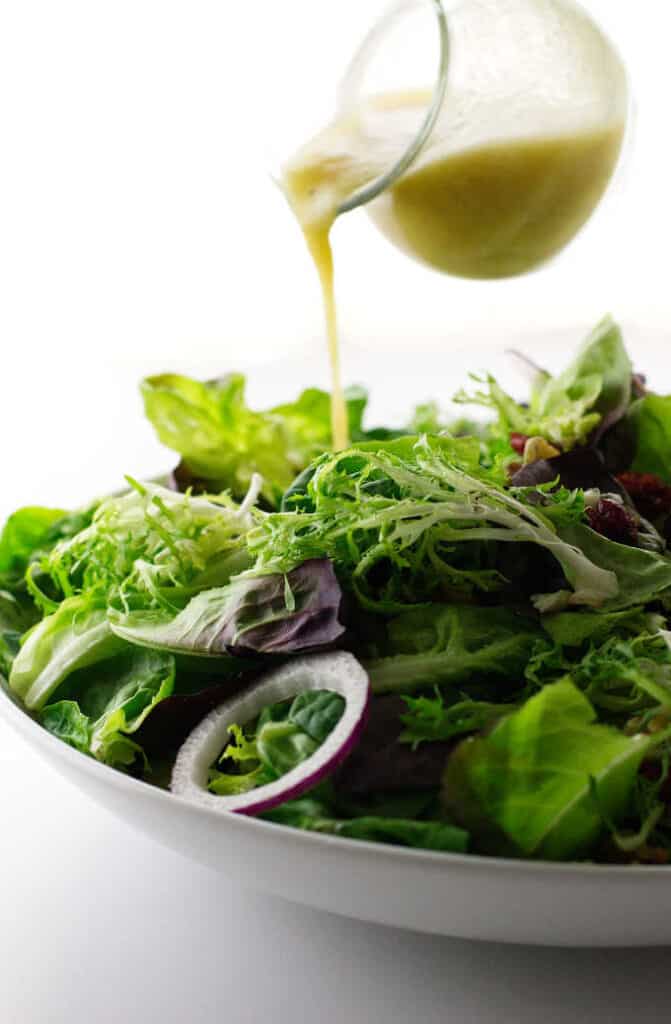 champagne vinaigrette being poured on bowl of salad