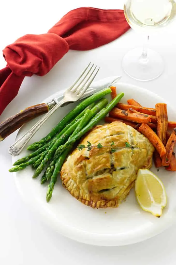 Overhead view of salmon and crab wellington with asparagus, carrots, lemon wedge and a glass of wine