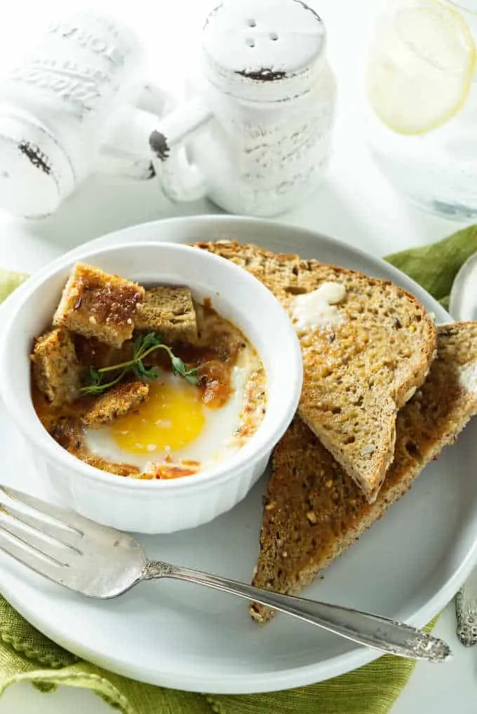 A serving of baked eggs with tomatoes in an individual ramekin.