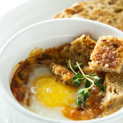 A baked egg with tomatoes in a white ramekin.