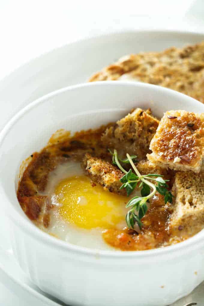 A baked egg with tomatoes in a white ramekin.