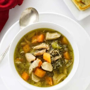 A bowl of vegetable chicken soup with wild rice and a plate of bread.