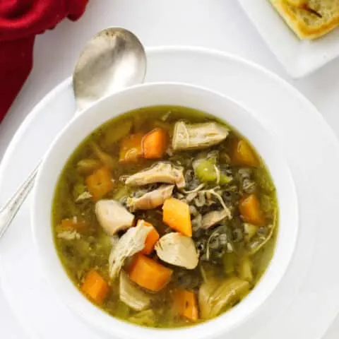 A bowl of vegetable chicken soup with wild rice and a plate of bread.