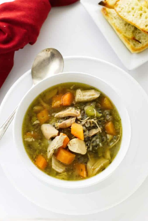 A bowl of vegetable chicken soup with wild rice and a plate of bread.