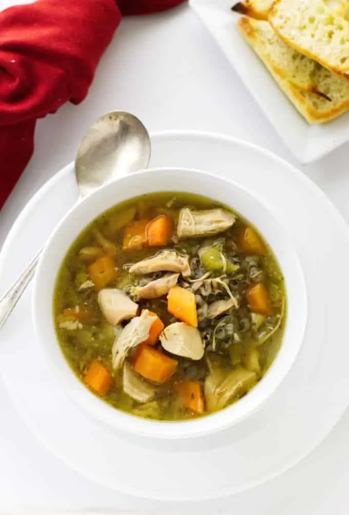 A bowl of vegetable chicken soup with wild rice and a plate of bread.
