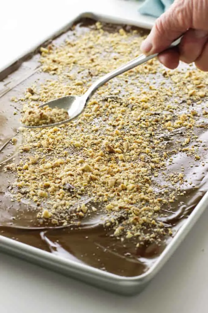 Pan of English toffee with nuts being sprinkled on top
