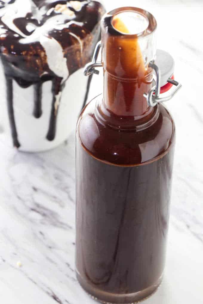 Homemade chocolate syrup and a cup of hot cocoa made with chocolate syrup.