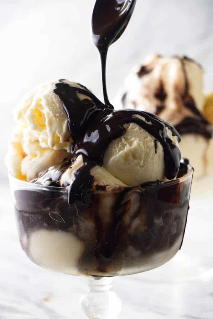 Chocolate syrup drizzled off a spoon onto ice cream.