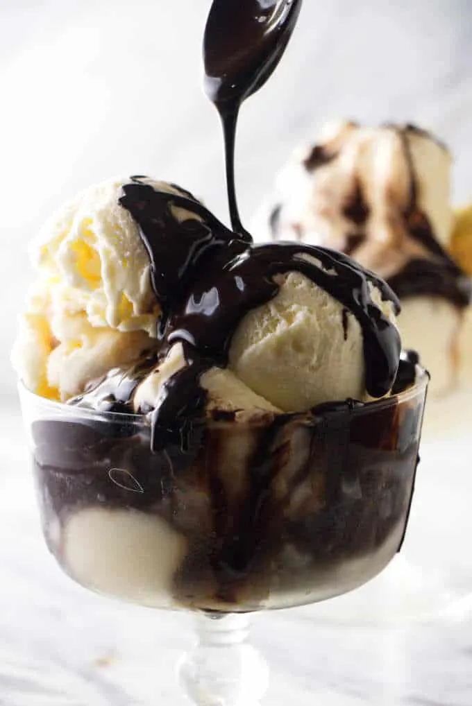 Chocolate syrup drizzled off a spoon onto ice cream.