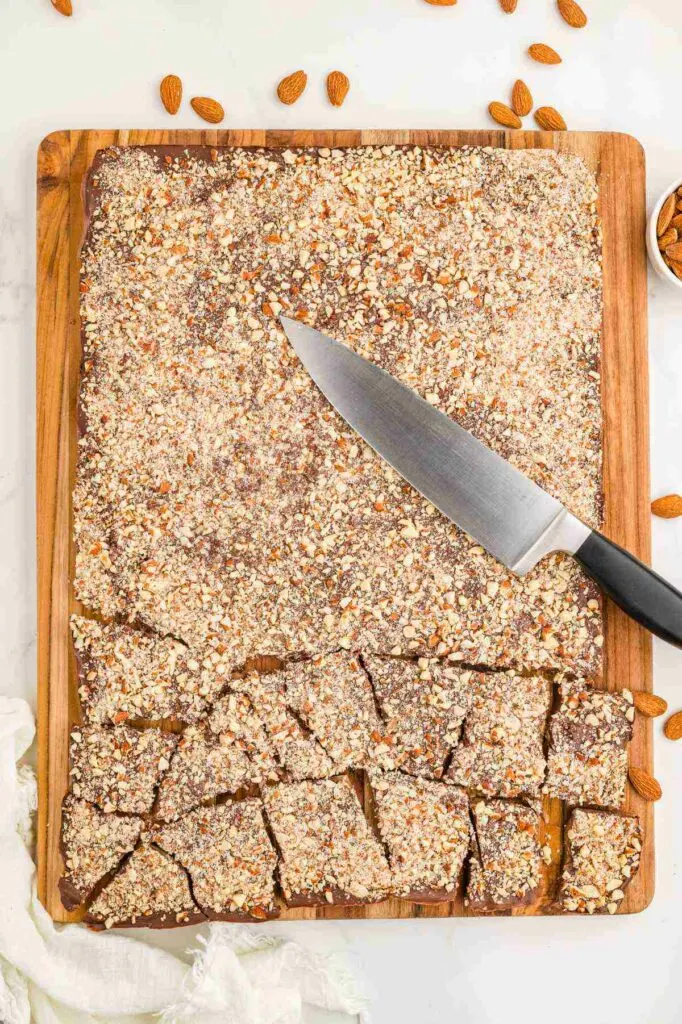 A knife on top of a block of almond toffee brittle that is partially broken into individual candies.