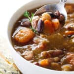 A spoon scooping up from a bowl of 15 bean soup.