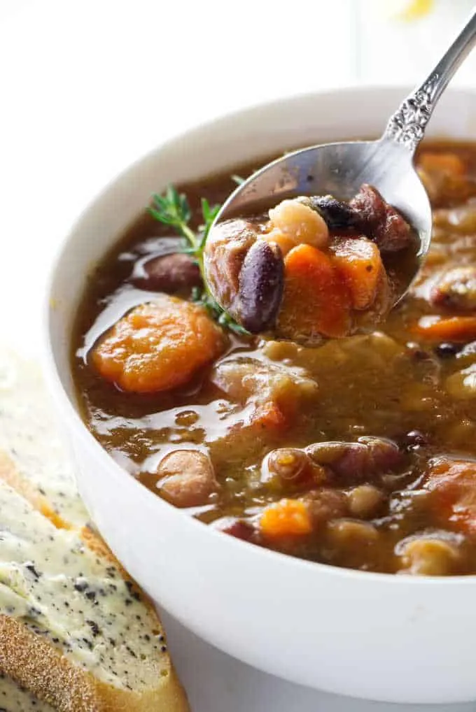 A spoon scooping up from a bowl of 15 bean soup.