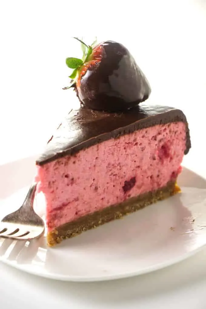 A slice of no-bake strawberry cheesecake covered in chocolate.