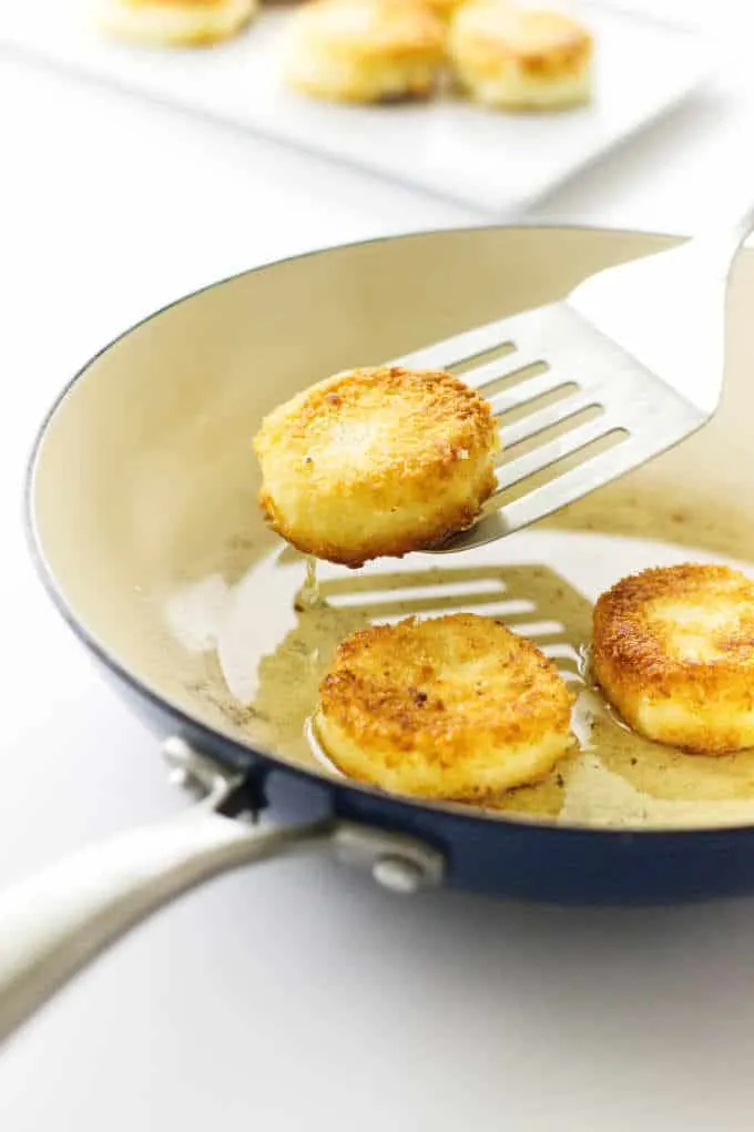 Breaded Goat cheese discs in skillet with spatula