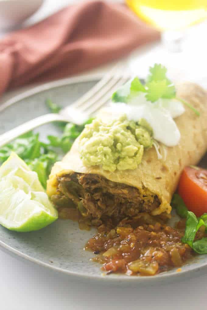 A shredded beef chimichanga on a plate with salsa and a slice of lime.