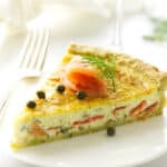 Serving of quiche on a plate with fork, napkin and wine in background