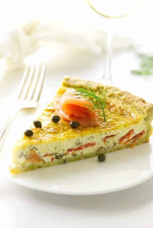 Serving of quiche on a plate with fork, napkin and wine in background