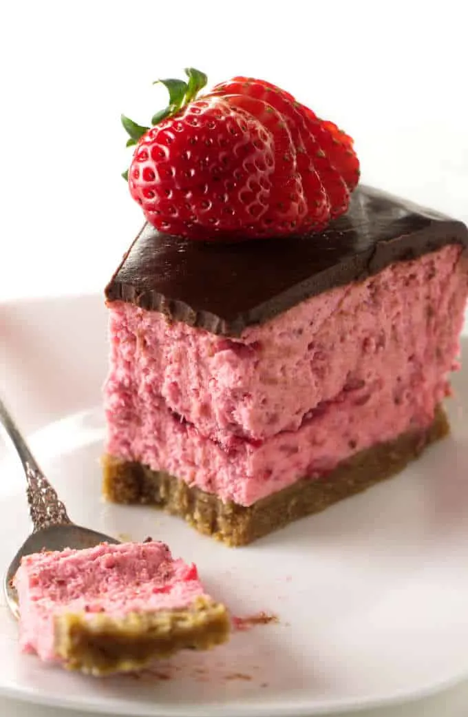 A partially eaten strawberry cheesecake with chocolate on top.