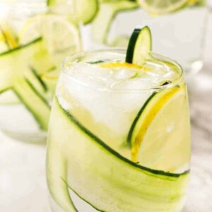 A glass of cucumber lemon water with a pitcher in the background.