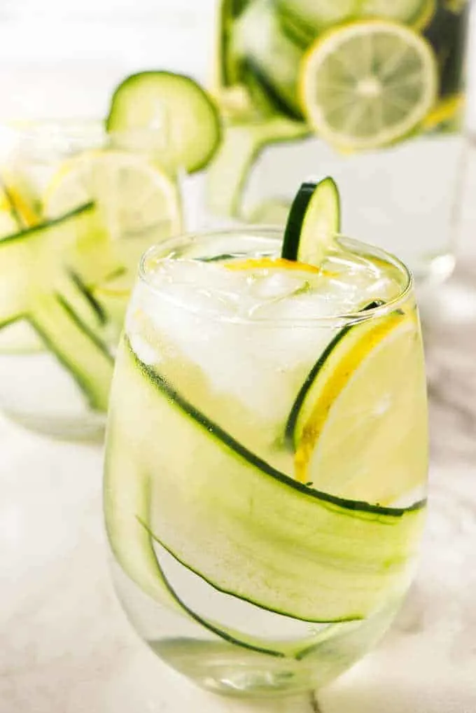 A glass of cucumber lemon water with a pitcher in the background.