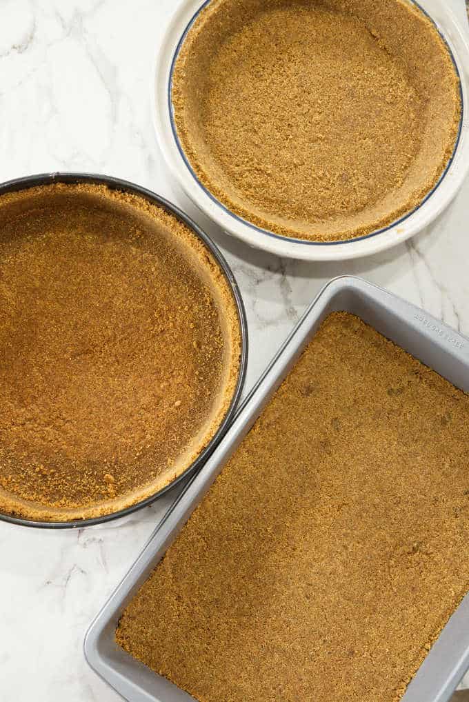 Graham cracker crust in a pie plate, a cheesecake pan, and a rectangle baking pan.