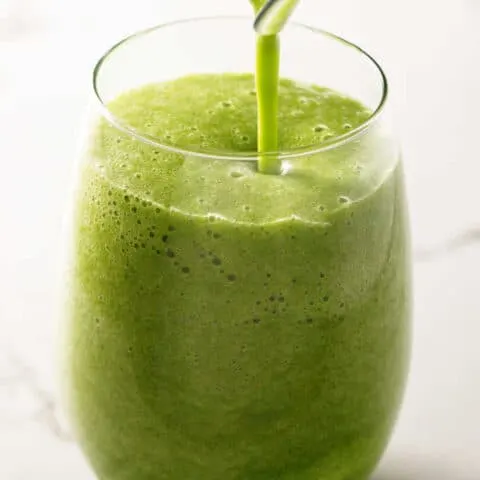 Pouring a green smoothie into a glass.