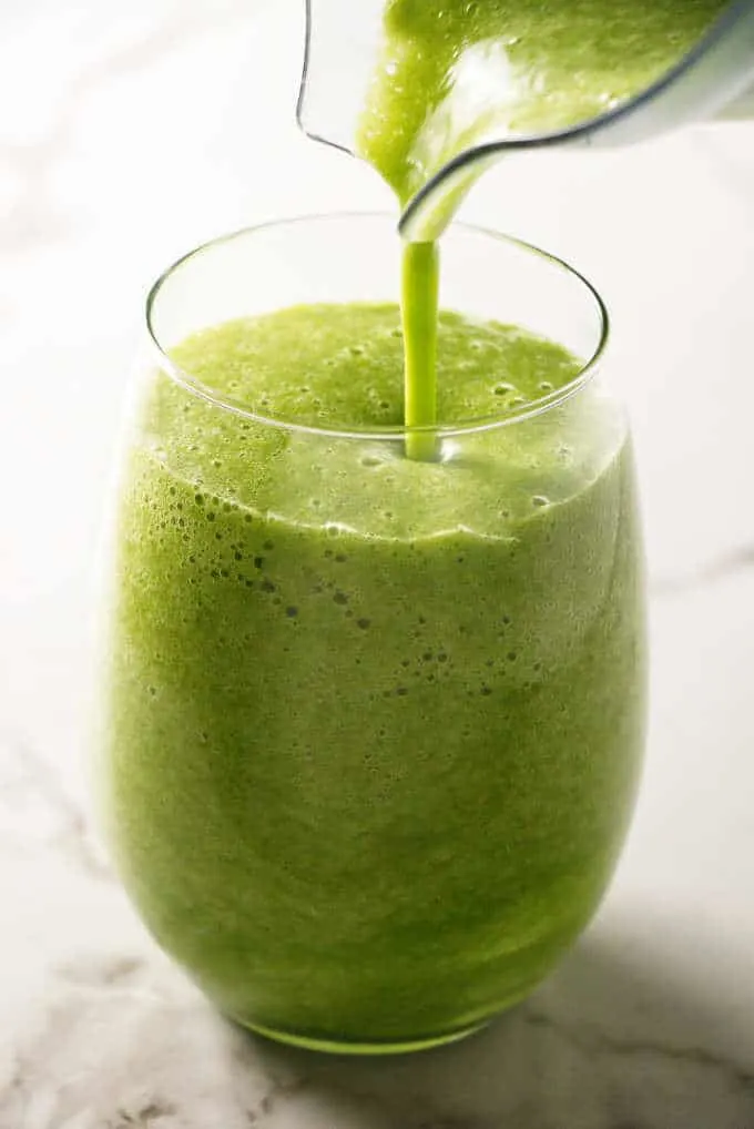 Pouring a green smoothie into a glass.