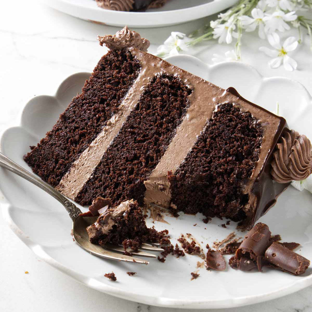 A slice of triple chocolate cake with three layers and chocolate buttercream.