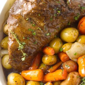 A tri tip in a serving dish with potatoes, carrots and onions.