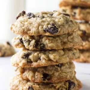 A tall stack of oatmeal raisin cookies with milk in the background.