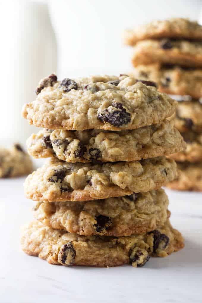 A tall stack of oatmeal raisin cookies with milk in the background.